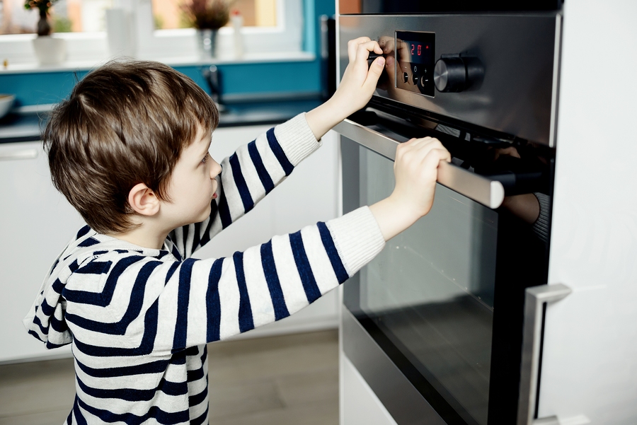 Boy Dangerously Playing With The Knobs On The Oven