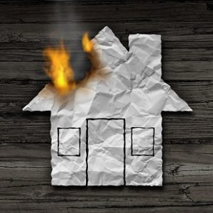 House fire concept and residential smoke disaster and burning destruction symbol as crumpled paper shaped as a family home residence as a 3D illustration on rustic wood.