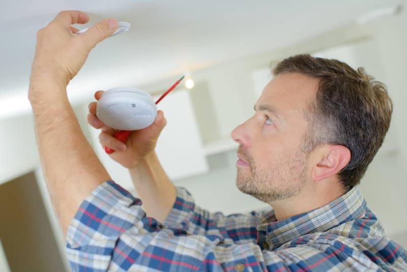 A homeowner performing a routine safety inspection on the smoke detector in his living room.