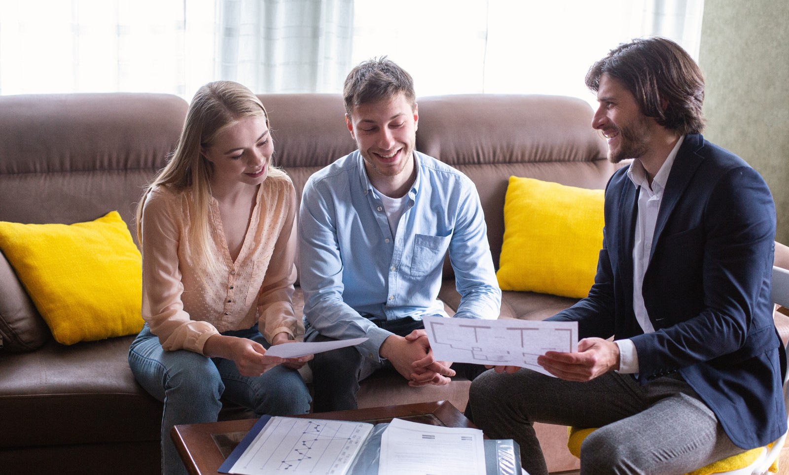 Happy couple with property manager looking at house plan indoors