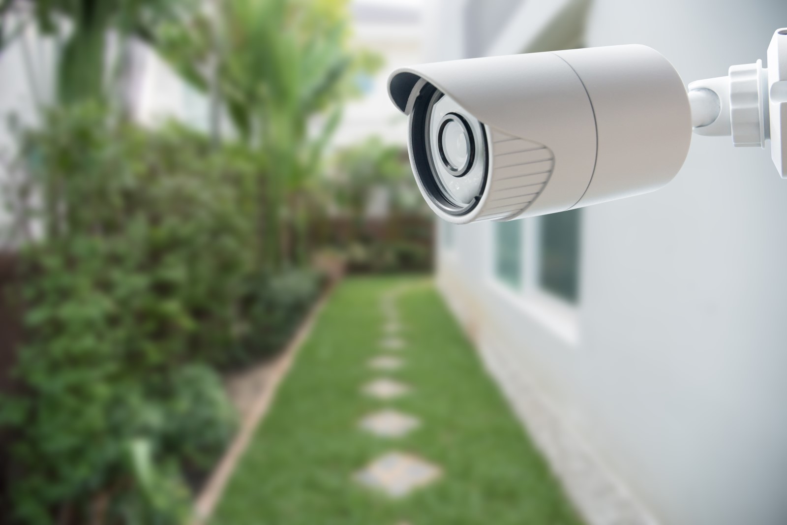 a home video surveillance system camera mounted on the exterior of a home near a grassy pathway