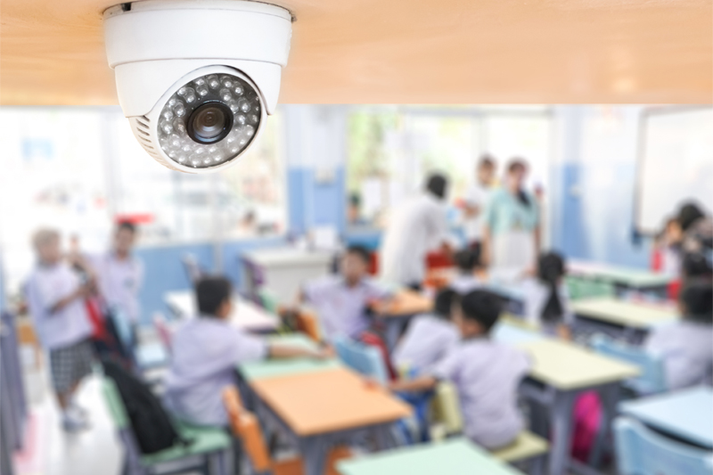 a blurred image of children at tables with a focus on the daycare center's security surveillance camera