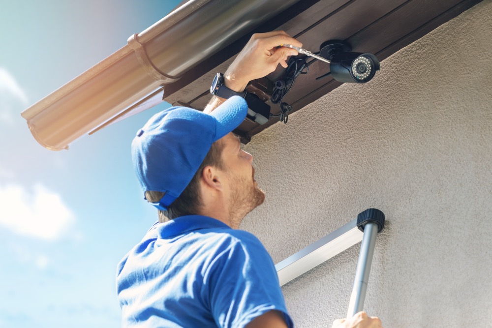 A technician installing a wireless outdoor home security camera system.
