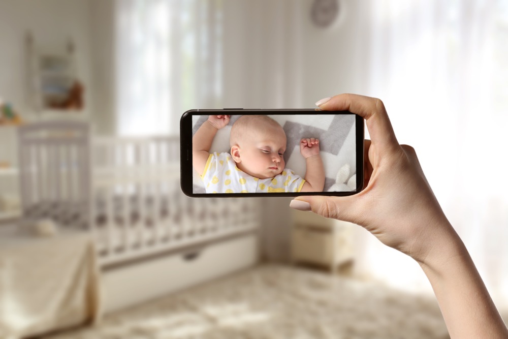A mother monitors her baby through her home security camera system and smartphone.