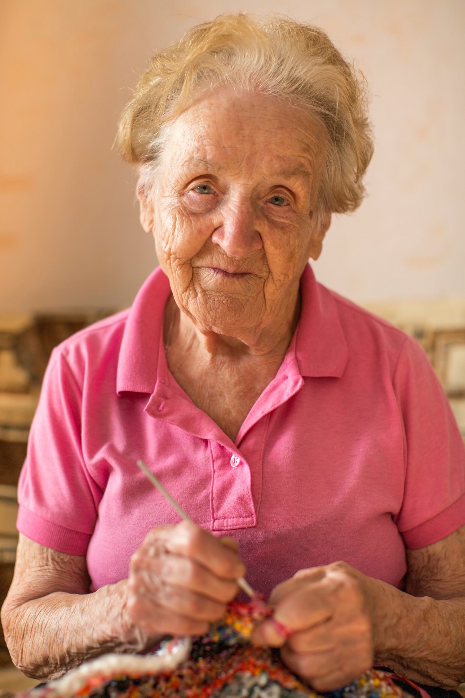 An elderly lady knitting and smiling because she's protected by a fire alarm system